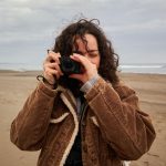 10 Moment Best-Selling Gear & Accessories - A woman holding a compact camera with beach in the background