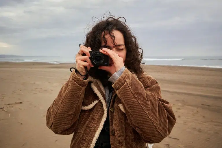 10 Moment Best-Selling Gear & Accessories - A woman holding a compact camera with beach in the background